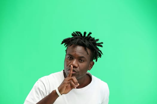 A man, close-up, on a green background, shows a sign of silence.
