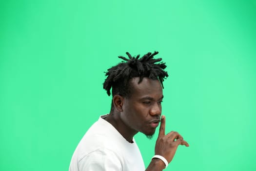 A man, close-up, on a green background, shows a sign of silence.