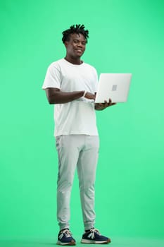 A man, full-length, on a green background, uses a laptop.