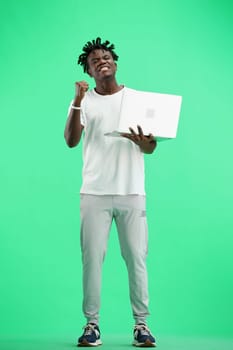 A man, full-length, on a green background, uses a laptop.