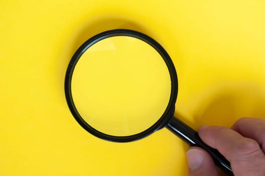 Top view of magnifying glass on yellow background with customizable space for text