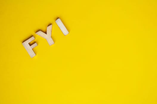 Top view of wooden FYI text on yellow background with customizable space for text.