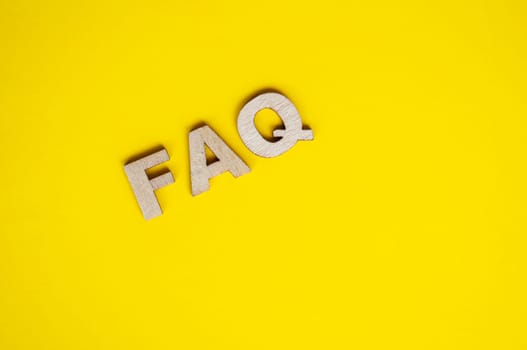 Top view of wooden FAQ text on yellow background. Frequently ask questions concept.