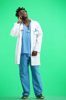 The doctor, in full height, on a green background, talking on the phone.