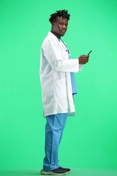 The doctor, in full height, on a green background, uses a phone.