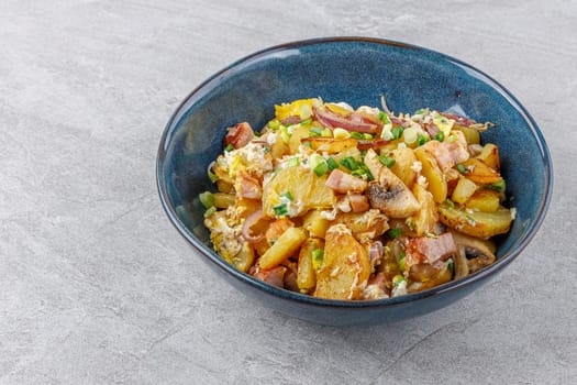fried potatoes with mushrooms and ham on a stone background studio food photo
