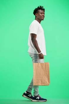 A man, full-length, on a green background, with bags, is walking.