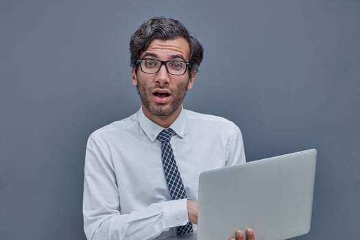 young successful man on a gray background typing in a laptop. surprised.