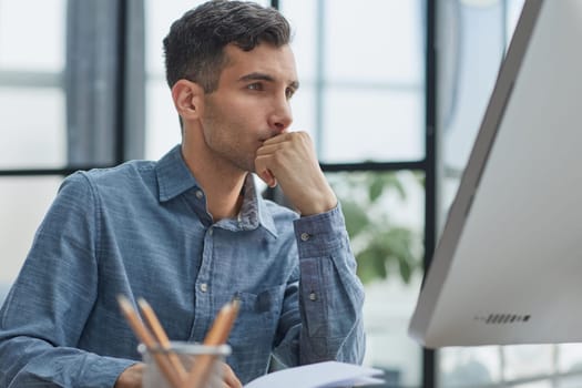 A young pensive man works in the office and thinks about something.