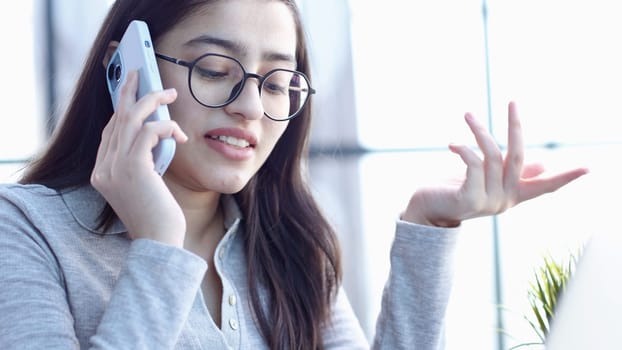 A young woman with glasses in the office talking on the phone.