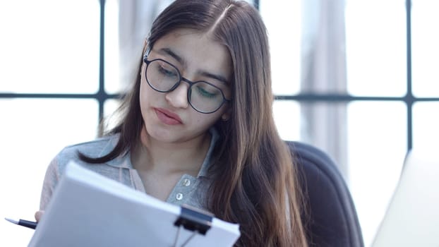 A young woman with glasses in the office is working with documents.