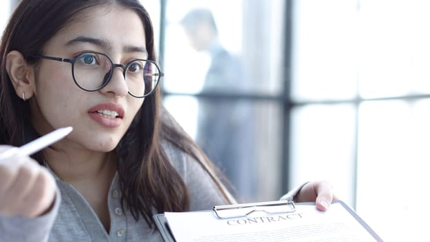 A young woman with glasses in the office discusses signing a contract.