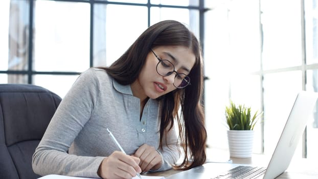 A young woman with glasses in the office is working on a laptop.