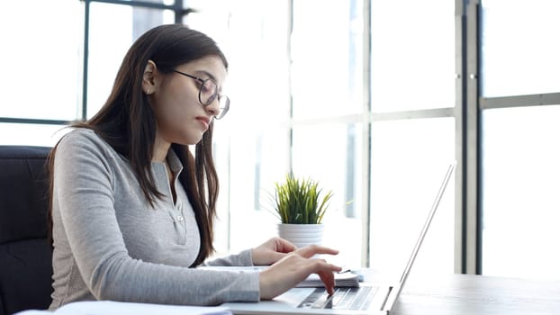 A young woman with glasses in the office is working with a laptop.