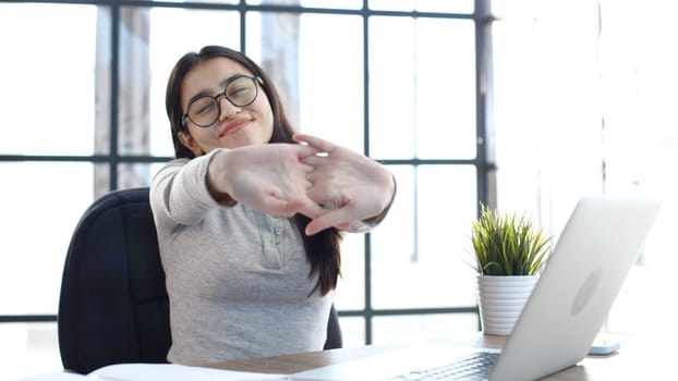 A young woman with glasses in the office is tired working at the computer.