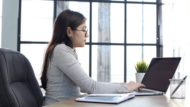A young woman with glasses in the office is working on a laptop.
