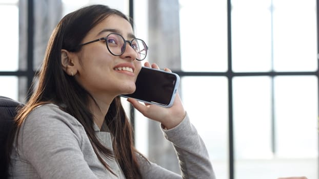 A young woman with glasses in the office talking on the phone.