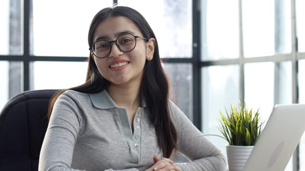 A young woman with glasses in the office looks at the camera.