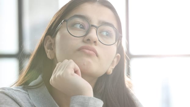 A young woman with glasses in the office is thinking.