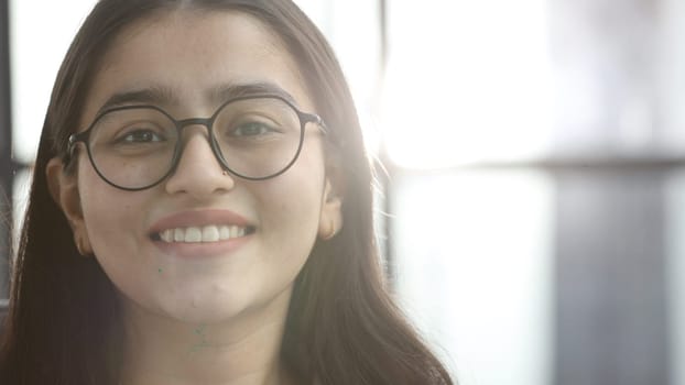 A young woman with glasses in the office looks at the camera.