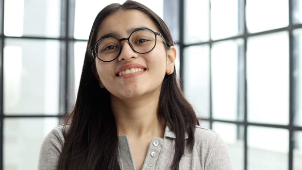 A young woman with glasses in the office looks at the camera.