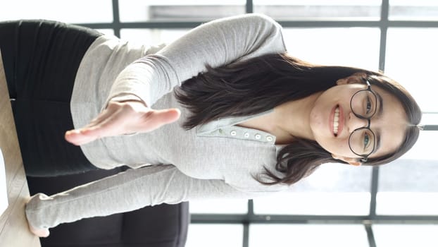 A young woman with glasses in the office looks at the camera.