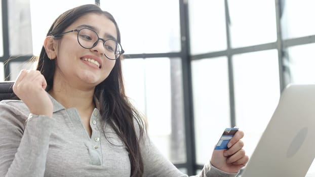 A young woman in close-up with glasses and a card in her hands thinks.