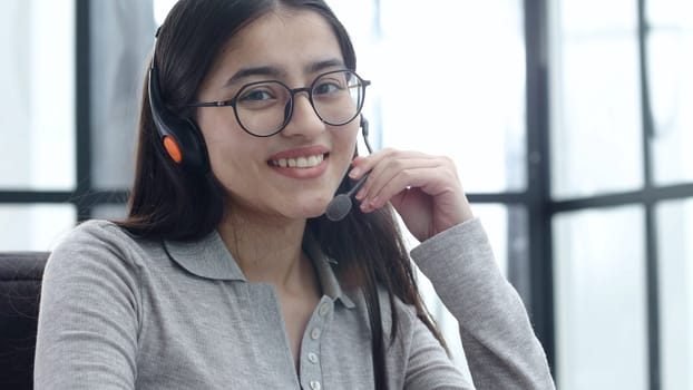 A young woman in close-up with glasses and headphones works in a call center.