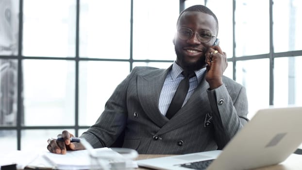 A businessman man in a jacket is talking on the phone in the office in close-up.