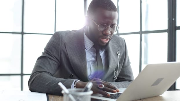 A businessman man in a close-up in a jacket, he works in the office with a laptop.