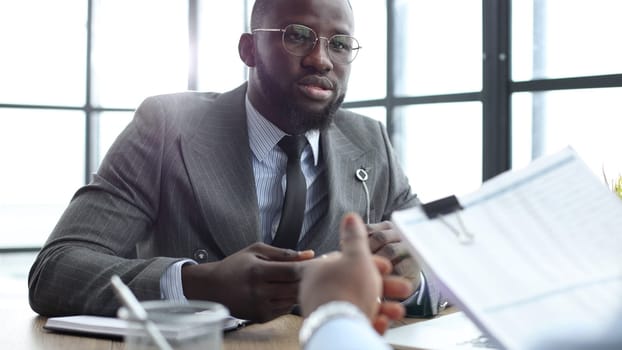 A businessman man in a close-up in a jacket discusses reports at an office meeting.