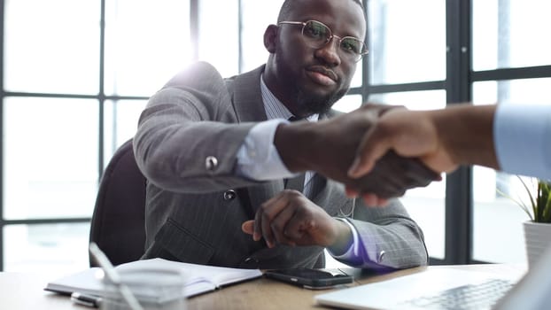 A businessman man in a close-up in a jacket shakes hands with a colleague in the office.