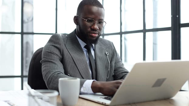 A businessman man in a close-up in a jacket working on a laptop in the office.