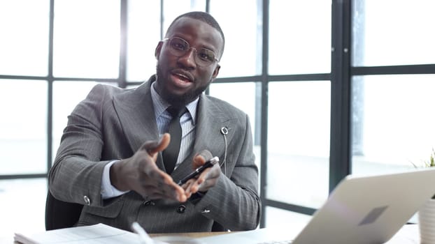 A businessman man in a close-up in a jacket speaks to the camera in the office.