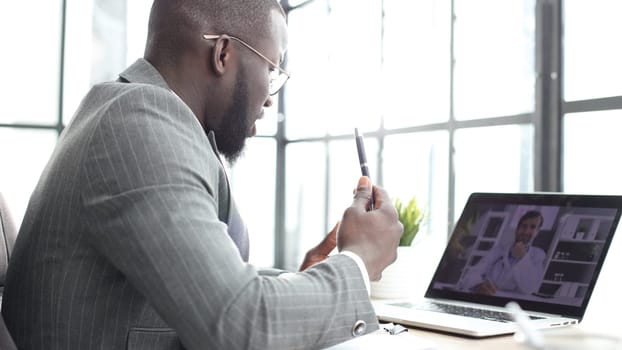 A businessman man in a close-up in a jacket in the office talking at an online meeting on a laptop.