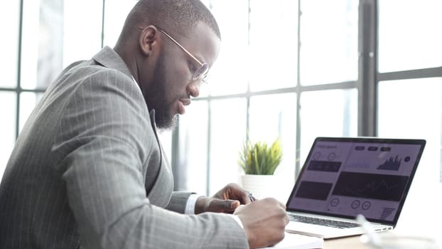 A businessman man in a close-up in a jacket in the office working with graphs on a laptop.