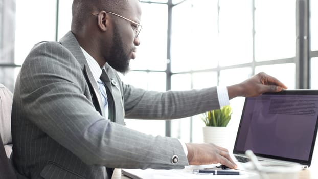A businessman man in a close-up in a jacket in the office working with graphs on a laptop.