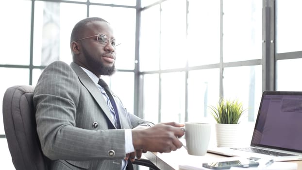 A businessman man in a close-up in a jacket in the office with a cup of coffee.