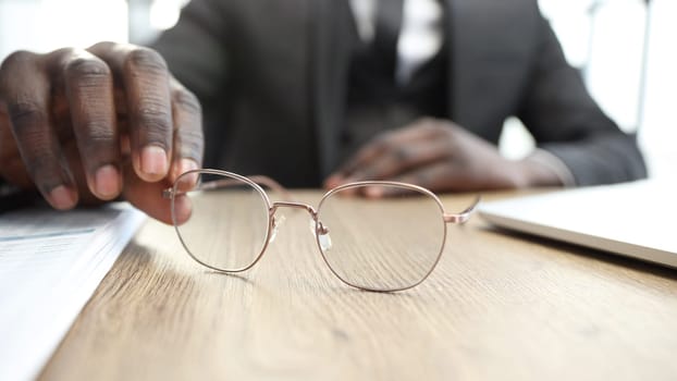 A businessman man in a close-up in a jacket in the office, he takes glasses.