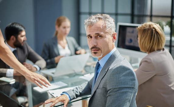 businessman against the background of his colleagues sitting at the table looks at the camera