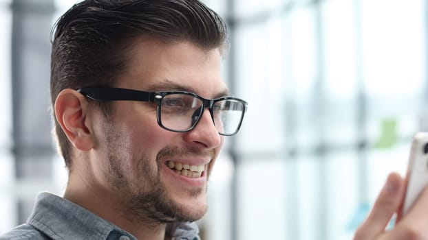 A man's face is in close-up with glasses, he uses a phone.