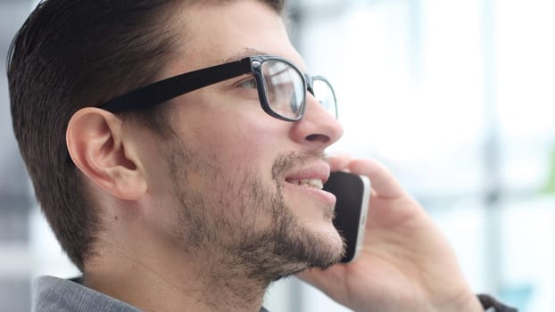 A man's face in glasses is in close-up, he is talking on the phone.