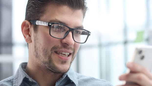 A man's face in glasses is in close-up, he is talking on the phone.