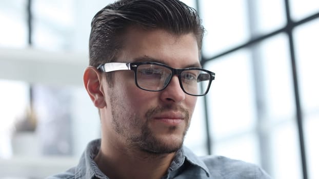 The man's face in glasses is in close-up, he looks thoughtfully away.