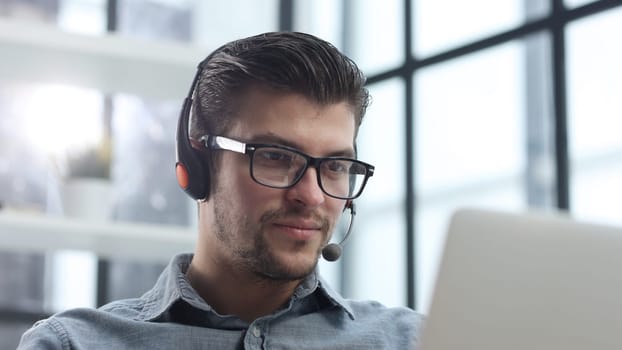 A man with headphones in close-up using a laptop.
