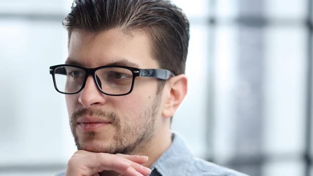 A man's face in close-up with glasses looks thoughtfully away.