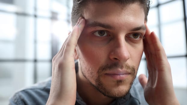 The man's face is in close-up, he is tired and has a headache.