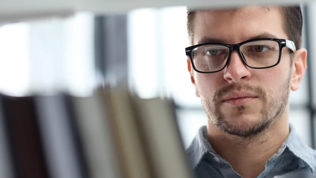 A man's face is in close-up with glasses, he is looking at books.