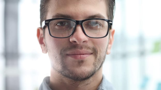 A man's face in close-up with glasses looks at the camera.