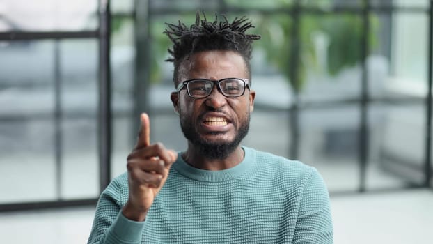 Portrait of a serious african american man, shaking his finger, warning and preventing you from something bad, looking at the camera with a worried expression.